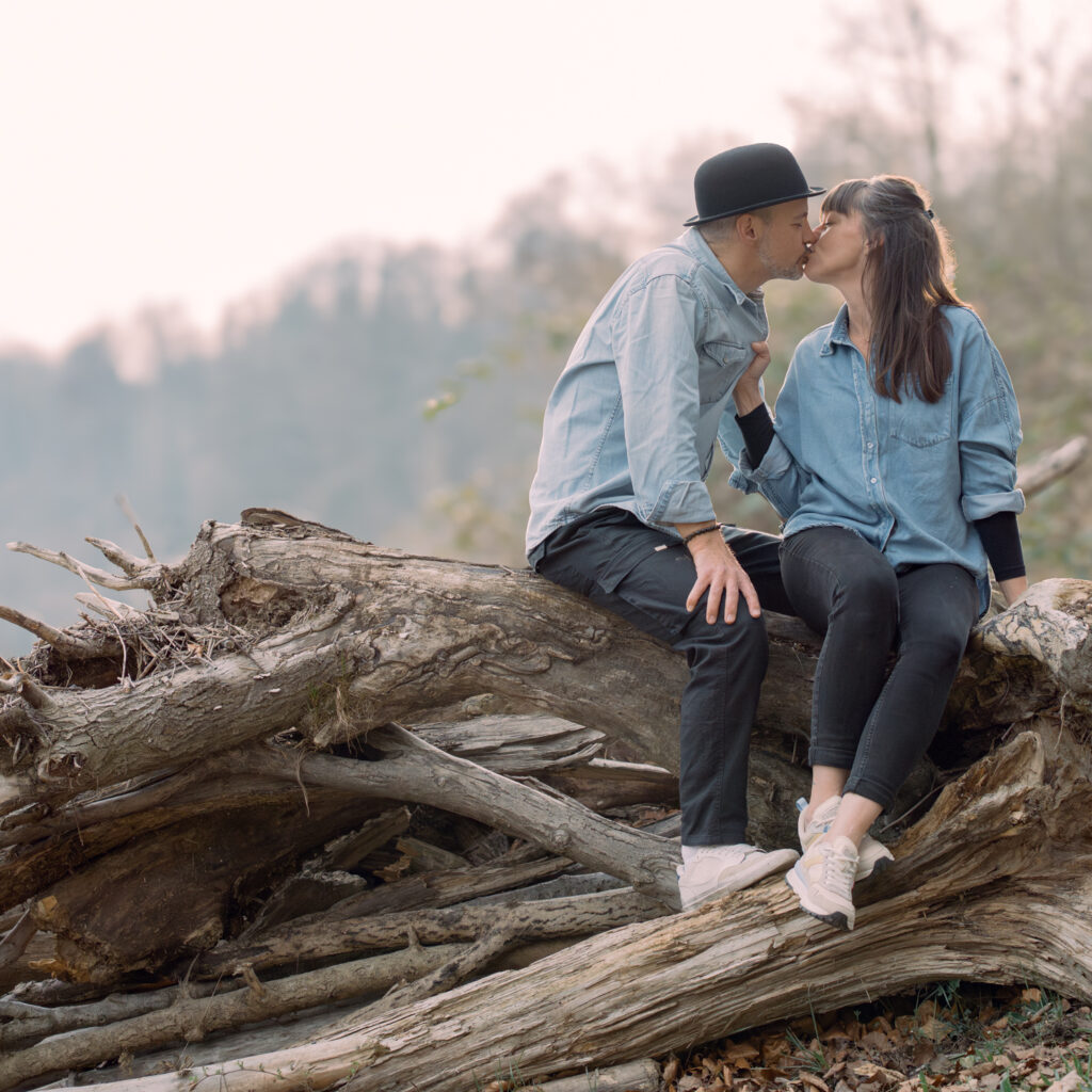 Frau küsst Mann und sitzen auf Baumstamm bei einem Paarshooting von einer Fotografin fotografiert